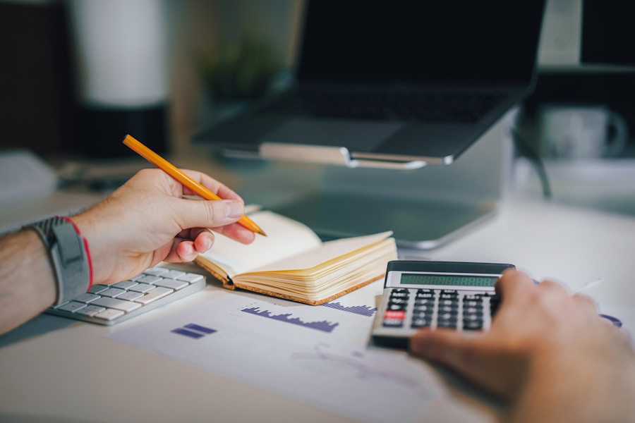 Alguien tomando notas junto a una calculadora, gráficos impresos y una computadora